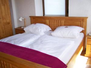 een groot bed met witte lakens en kussens bij Anna Ferienwohnung am Eifelsteig in Neroth