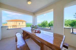 a large porch with a wooden table and large windows at Apartmani Željka in Krk