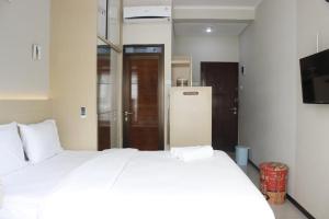 a bedroom with a white bed and a refrigerator at Homey Studio Gateway Pasteur Apartment near Exit Toll By Travelio in Bandung