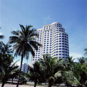 a tall building with palm trees in front of it at Hainan Junhua Haiyi Hotel (Formerly Meritus Mandarin Haikou) in Haikou