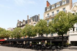 a group of tables and chairs with umbrellas and trees at Hôtel Bristol Reims in Reims