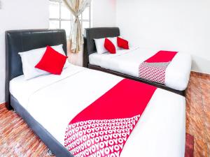 two beds with red and white pillows in a room at D' Anjung Inn in Tangkak