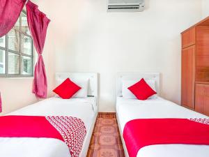 two twin beds in a room with red pillows at D' Anjung Inn in Tangkak