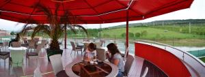Duas raparigas sentadas numa mesa debaixo de um guarda-chuva vermelho em Prity Sport Botique Hotel em Gorna Oryakhovitsa