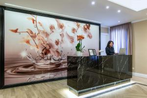 una mujer de pie en un escritorio en un vestíbulo con un gran mural de flores en The Boutique Hotel en Roma