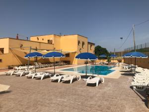 uma piscina com cadeiras brancas e guarda-sóis azuis em Baglio Pocoroba em Calatafimi