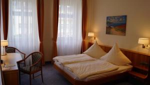 a bedroom with a bed and a chair and two windows at Hotel Goldener Löwe in Waldheim