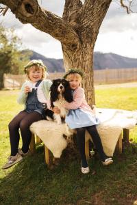 two young girls sitting on a bench with a dog at Tourist Farm Urška in Zreče