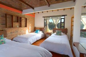 3 camas en una habitación con una pared de ladrillo en Casa de las Palmas en Villa de Leyva