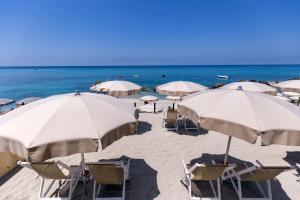 einen Strand mit weißen Sonnenschirmen und Stühlen sowie das Meer in der Unterkunft Villaggio Tramonto in Capo Vaticano