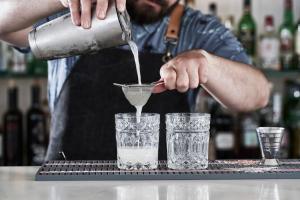 a man pouring a drink into two glasses on a bar at Antigoni Seaside Resort in Ormos Panagias