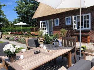 a wooden table with chairs and an umbrella at Eidumhaus, freistehendes Reetdachhaus mit Garten in Strandnähe in Westerland (Sylt)