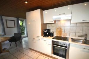 cocina con armarios blancos, fregadero y fogones en Kleines Haus mitten in der Natur mit eigener Terrasse und Sonnenbalkon, en Halver