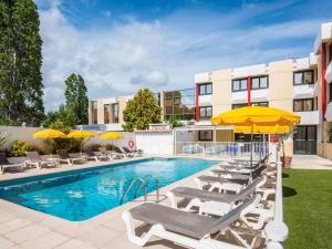 uma piscina com espreguiçadeiras e guarda-sóis em ibis Styles Nice Cap 3000 Aéroport em Saint-Laurent-du-Var