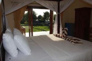 Un dormitorio con una cama blanca con almohadas y una ventana. en Taman Padi Villa, en Amed