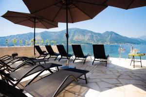 a group of chairs and umbrellas on a patio next to the water at Hotel Sara in Kotor