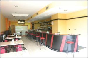 a restaurant with a bar with red chairs and tables at Albergue La Encina in Hospital de Órbigo