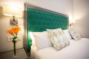 a bed with a green headboard and a vase with a flower at Plazuela del Carbón Suites in Cádiz