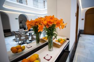 two vases with orange flowers on a table with fruit at Plazuela del Carbón Suites in Cádiz