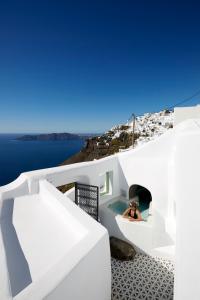 una persona è seduta in una piscina su una casa bianca di Gitsa Cliff Luxury Villa a Imerovigli