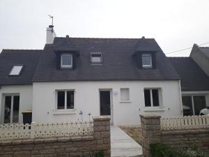 een wit huis met een zwart dak en een hek bij les quatres vents in Santec