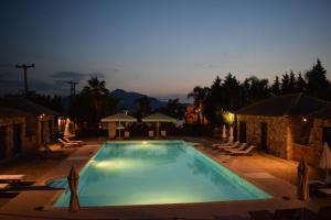 een groot zwembad 's nachts met stoelen en bomen bij Almyra Holiday Village in Edipsos