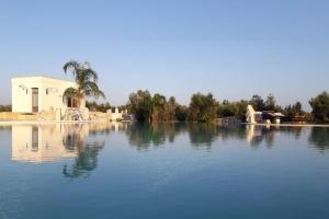 a large lake with a building and a palm tree at Agriturismo Le Site in Corigliano dʼOtranto