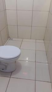 a bathroom with a toilet in a white tiled floor at Pousada Alvorada in Riachão
