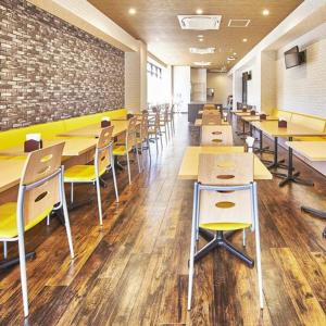 a cafeteria with tables and chairs and a brick wall at The Celecton Kitamoto Ekimae in Kitamoto