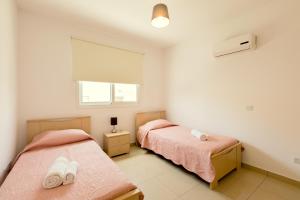 two beds in a bedroom with pink sheets and a window at Oceania Bay Village in Pyla