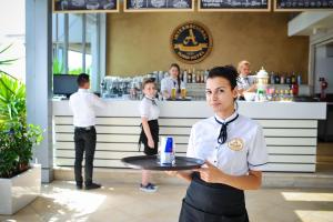 una camarera sosteniendo una bandeja delante de un bar en Iliria Internacional Hotel, en Durrës