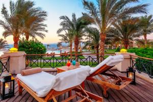 a deck with two chairs and a table and palm trees at Cleopatra Luxury Resort Sharm El Sheikh in Sharm El Sheikh