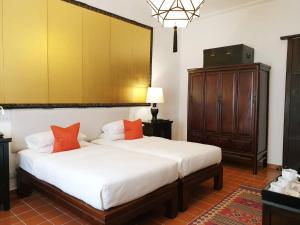 Rachamankha Hotel في شيانغ ماي: غرفة نوم بسرير وملاءات بيضاء ومخدات برتقالية