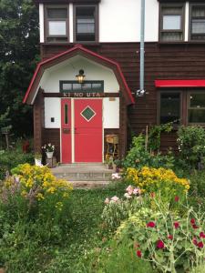 a red door on the front of a house with flowers at Pension Kinouta in Biei