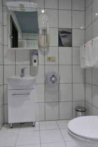 a white tiled bathroom with a toilet and a sink at Alex Hotel on Dybenko in Saint Petersburg