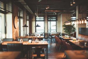 a restaurant with wooden tables and chairs and windows at Fliegerdeich Hotel & Restaurant in Wilhelmshaven