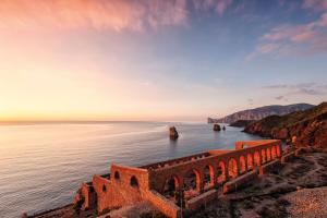 an old stone bridge over the ocean at sunset at Bed and Breakfast Porto Flavia in Iglesias