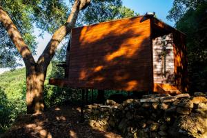a wooden cabin next to a tree and a stone wall at Caparica Azores Ecolodge in Biscoitos