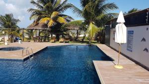 a swimming pool with a umbrella and palm trees at Village Praia de Itacimirim in Itacimirim