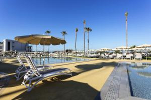 a swimming pool with lounge chairs and an umbrella and a swimming pool at Hipotels Barrosa Park in Chiclana de la Frontera