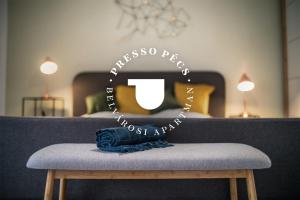 a room with a bed with a bench with a sign at Presso Pécs in Pécs