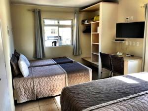 a hotel room with two beds and a desk and a television at Pousada Mar Do Leste in Florianópolis