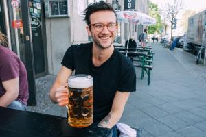 Un uomo seduto a un tavolo con una birra in mano di St Christopher's Inn Berlin Alexanderplatz a Berlino