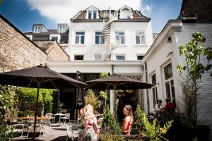 eine Gruppe von Personen, die unter Sonnenschirmen vor einem Gebäude sitzen in der Unterkunft Fitz Roy Urban Hotel, Bar and Garden in Maastricht