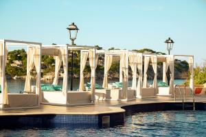 Sentido Fido Punta del Mar Hotel & Spa - Adults Only في سانتا بونسا: صف من الكراسي البيضاء على رصيف في الماء