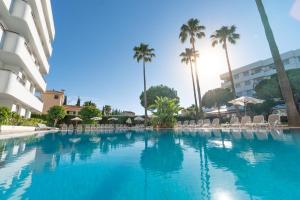 a large swimming pool with chairs and palm trees at Tropicana Hotel in Cala Millor