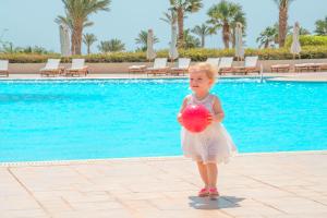 a little girl holding a ball in front of a pool at Kempinski Hotel Soma Bay in Hurghada