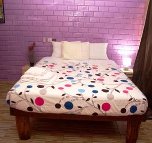 a bed with a floral comforter with a purple wall at Residence Hotel Lwili in Ouagadougou