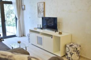 sala de estar con TV de pantalla plana en un centro de entretenimiento blanco en Brand New Apartments en Sveti Stefan