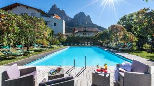 a swimming pool with chairs and a house and mountains at Activehotel Diana in Siusi